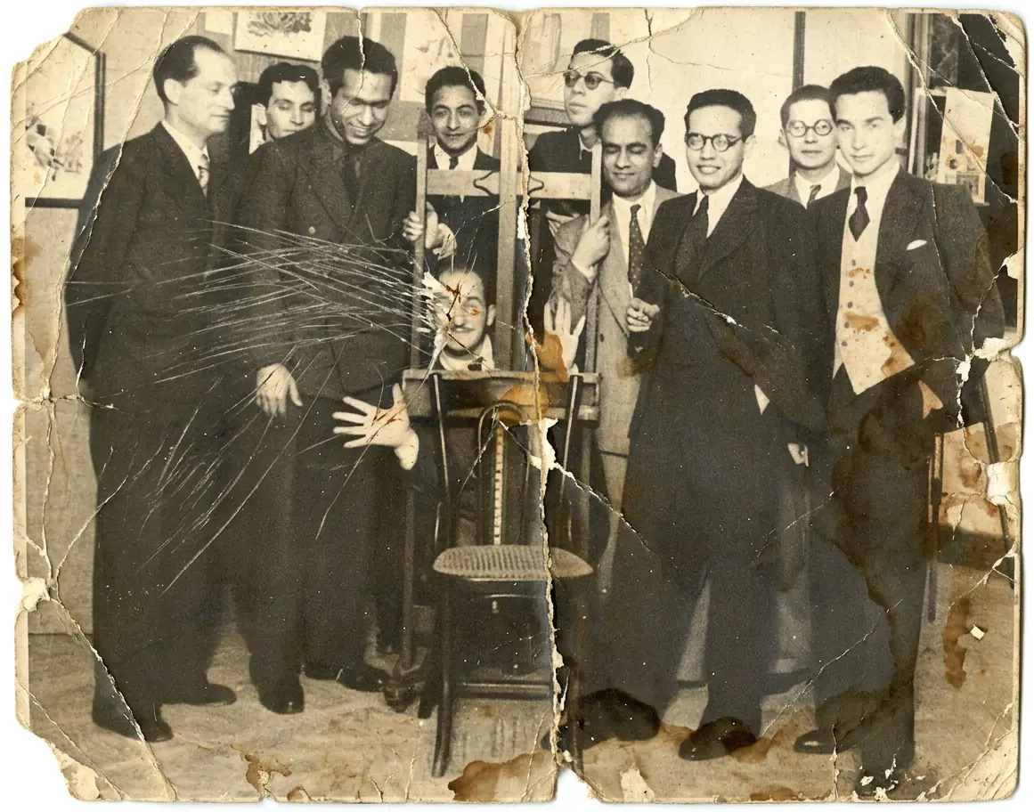 A group of friends gathered around a chair, the print scratched right across the middle - the scratches gone and the suits in color